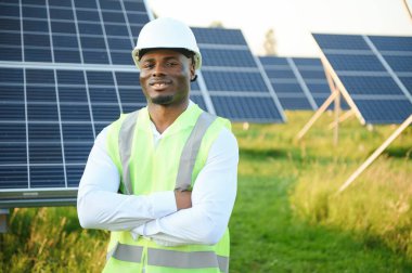 Beyaz gömlekli ve şapkalı Afro-Amerikalı bir mühendis güneş panelleri üzerinde çalışıyor. Güneş enerjisi yenilenebilir enerji kavramı