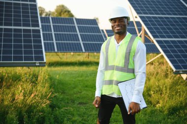 Genç, yakışıklı Afrikalı Amerikalı zanaatkârın yakın portresi koruyucu bir miğfer. Tulumlu, kameraya gülümseyen mutlu bir adam. Yavaş çekim