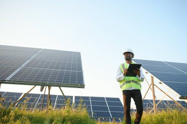 Afrikalı Amerikalı teknisyen güneş panellerinin bakımını kontrol ediyor. Güneş istasyonundaki siyah adam mühendisi.