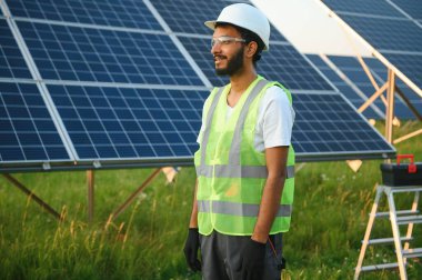 Yeşil yelekli Hintli bir erkek mühendis güneş panelleri üzerinde çalışıyor. Yenilenebilir enerji kavramı