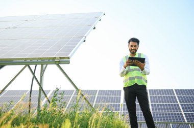 Genç Hintli erkek mühendisin portresi güneş panellerinin yanında duruyor, açık mavi gökyüzü arka planı, yenilenebilir ve temiz enerjisi var. beceri Hindistan, kopyalama alanı