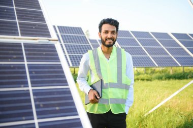 Genç Hintli erkek mühendisin portresi güneş panellerinin yanında duruyor, açık mavi gökyüzü arka planı, yenilenebilir ve temiz enerjisi var. beceri Hindistan, kopyalama alanı