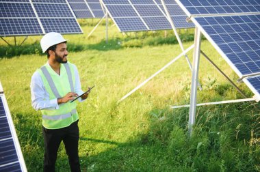 Genç Hintli erkek mühendisin portresi güneş panellerinin yanında duruyor, açık mavi gökyüzü arka planı, yenilenebilir ve temiz enerjisi var. beceri Hindistan, kopyalama alanı