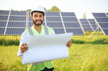 Genç Hintli erkek mühendisin portresi güneş panellerinin yanında duruyor, açık mavi gökyüzü arka planı, yenilenebilir ve temiz enerjisi var. beceri Hindistan, kopyalama alanı