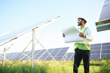 Genç Hintli erkek mühendisin portresi güneş panellerinin yanında duruyor, açık mavi gökyüzü arka planı, yenilenebilir ve temiz enerjisi var. beceri Hindistan, kopyalama alanı