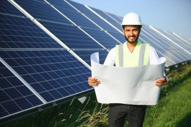 Genç Hintli teknisyen ya da yönetici güneş panelinin yanında duran resmi giysiler giyiyor. Yenilenebilir enerji, çapraz duran adam, boşluğu kopyala.