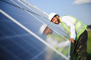 Genç Hintli teknisyen ya da yönetici güneş panelinin yanında duran resmi giysiler giyiyor. Yenilenebilir enerji, çapraz duran adam, boşluğu kopyala.