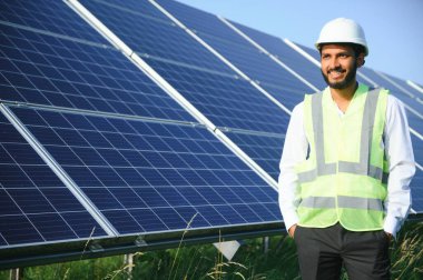 Genç Hintli teknisyen ya da yönetici güneş panelinin yanında duran resmi giysiler giyiyor. Yenilenebilir enerji, çapraz duran adam, boşluğu kopyala.