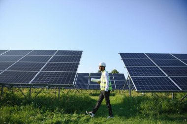 Genç Hintli teknisyen ya da yönetici güneş panelinin yanında duran resmi giysiler giyiyor. Yenilenebilir enerji, çapraz duran adam, boşluğu kopyala.