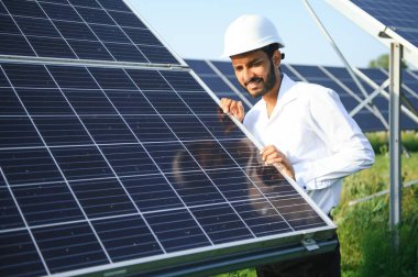 Genç Hintli teknisyen ya da yönetici güneş panelinin yanında duran resmi giysiler giyiyor. Yenilenebilir enerji, çapraz duran adam, boşluğu kopyala.