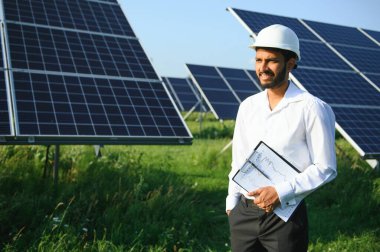 Genç Hintli erkek mühendisin portresi güneş panellerinin yanında duruyor, açık mavi gökyüzü arka planı, yenilenebilir ve temiz enerjisi var. beceri Hindistan, kopyalama alanı