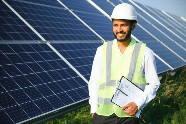 Genç Hintli teknisyen ya da yönetici güneş panelinin yanında duran resmi giysiler giyiyor. Yenilenebilir enerji, çapraz duran adam, boşluğu kopyala.