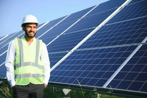 Yeşil yelekli Hintli bir erkek mühendis güneş panelleri üzerinde çalışıyor. Yenilenebilir enerji kavramı