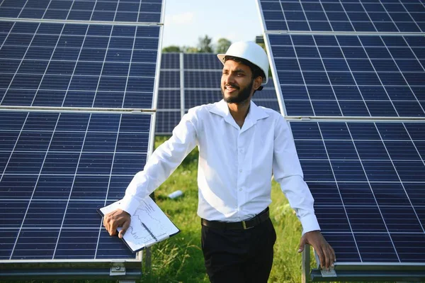 Genç Hintli erkek mühendisin portresi güneş panellerinin yanında duruyor, açık mavi gökyüzü arka planı, yenilenebilir ve temiz enerjisi var. beceri Hindistan, kopyalama alanı