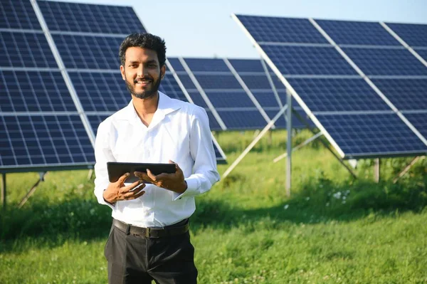 Genç Hintli erkek mühendisin portresi güneş panellerinin yanında duruyor, açık mavi gökyüzü arka planı, yenilenebilir ve temiz enerjisi var. beceri Hindistan, kopyalama alanı