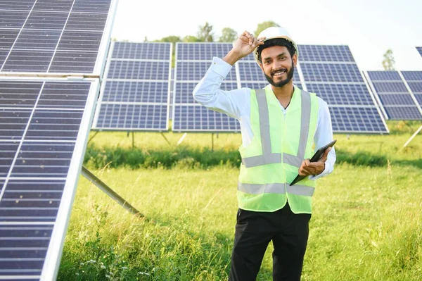 Yeşil yelekli Hintli bir erkek mühendis güneş panelleri üzerinde çalışıyor. Yenilenebilir enerji kavramı