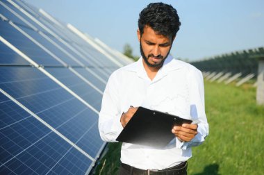 Genç Hintli teknisyen ya da yönetici güneş panelinin yanında duran resmi giysiler giyiyor. Yenilenebilir enerji, çapraz duran adam, boşluğu kopyala.