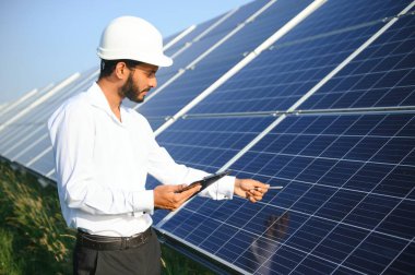 Genç Hintli teknisyen ya da yönetici güneş panelinin yanında duran resmi giysiler giyiyor. Yenilenebilir enerji, çapraz duran adam, boşluğu kopyala.