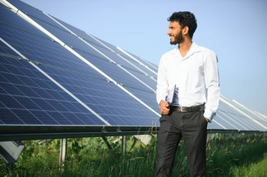 Güneş panellerinin yanında duran tabletli genç erkek mühendis, temiz mavi gökyüzü geçmişe sahip tarım arazisi, yenilenebilir enerji, temiz enerji