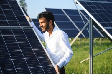 Yeşil yelekli Hintli bir erkek mühendis güneş panelleri üzerinde çalışıyor. Yenilenebilir enerji kavramı