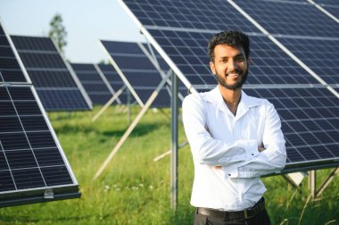 Genç Hintli teknisyen ya da yönetici güneş panelinin yanında duran resmi giysiler giyiyor. Yenilenebilir enerji, çapraz duran adam, boşluğu kopyala.