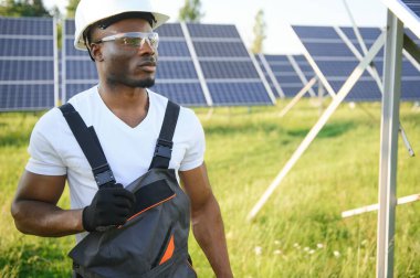 Güneş pili panellerini koruyan Afrikalı Amerikalı mühendis. Ekolojik güneş çiftliği inşaatında çalışan bir teknisyen. Yenilenebilir temiz enerji teknolojisi kavramı.