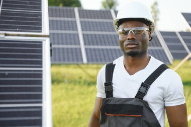 Güvenlik kaskı ve üniforma takan Afro-Amerikan elektrik mühendisinin portresi güneş panelleri kuruyor.
