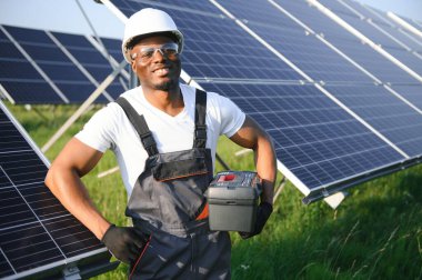 Güvenlik kaskı ve üniforma takan Afro-Amerikan elektrik mühendisinin portresi güneş panelleri kuruyor.