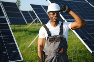 Güvenlik kaskı ve üniforma takan Afro-Amerikan elektrik mühendisinin portresi güneş panelleri kuruyor.