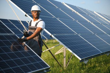 Güneş pili panellerini koruyan Afrikalı Amerikalı mühendis. Ekolojik güneş çiftliği inşaatında çalışan bir teknisyen. Yenilenebilir temiz enerji teknolojisi kavramı.