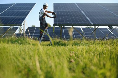 Güvenlik kaskı ve üniforma takan Afro-Amerikan elektrik mühendisinin portresi güneş panelleri kuruyor.