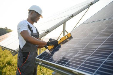 Güneş pili panellerini koruyan Afrikalı Amerikalı mühendis. Ekolojik güneş çiftliği inşaatında çalışan bir teknisyen. Yenilenebilir temiz enerji teknolojisi kavramı.