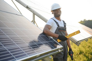 Güneş pili panellerini koruyan Afrikalı Amerikalı mühendis. Ekolojik güneş çiftliği inşaatında çalışan bir teknisyen. Yenilenebilir temiz enerji teknolojisi kavramı.