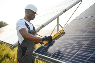 Güvenlik kaskı ve üniforma takan Afro-Amerikan elektrik mühendisinin portresi güneş panelleri kuruyor.