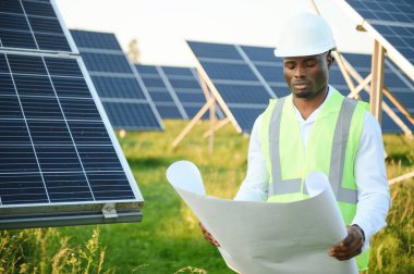 Afrikalı Amerikalı teknisyen güneş panellerinin bakımını kontrol ediyor. Güneş istasyonundaki siyah adam mühendisi.