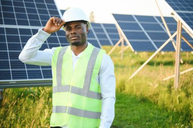 Genç, yakışıklı Afrikalı Amerikalı zanaatkârın yakın portresi koruyucu bir miğfer. Tulumlu, kameraya gülümseyen mutlu bir adam. Yavaş çekim