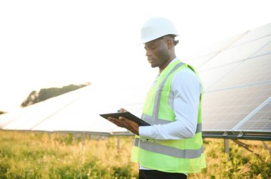 Genç, yakışıklı Afrikalı Amerikalı zanaatkârın yakın portresi koruyucu bir miğfer. Tulumlu, kameraya gülümseyen mutlu bir adam. Yavaş çekim