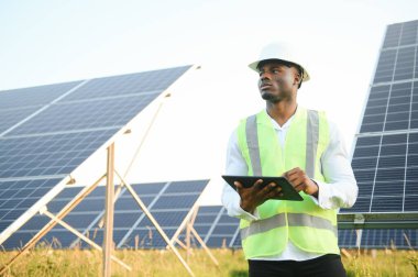 Genç, yakışıklı Afrikalı Amerikalı zanaatkârın yakın portresi koruyucu bir miğfer. Tulumlu, kameraya gülümseyen mutlu bir adam. Yavaş çekim