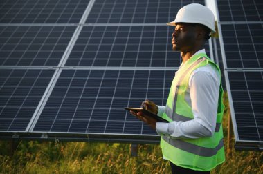 Genç, yakışıklı Afrikalı Amerikalı zanaatkârın yakın portresi koruyucu bir miğfer. Tulumlu, kameraya gülümseyen mutlu bir adam. Yavaş çekim