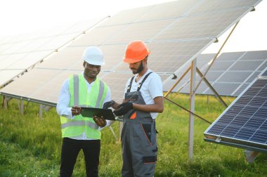 Güvenlik kasklı çok ırklı bir grup insan güneş istasyonunda duruyor ve ellerinde büyük çizimler olan kameralara bakıyor. İki mühendis ve teknisyen dışarıdaki panelleri inceliyor..