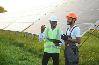 Güneş panellerindeki çok ırklı mühendisler. Afrika kökenli Amerikalı ve Arap mühendis güneş paneli çiftliğinde çalışıyor.
