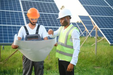Güneş panellerindeki çok ırklı mühendisler. Afrika kökenli Amerikalı ve Arap mühendis güneş paneli çiftliğinde çalışıyor.