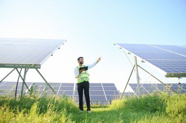 Genç Hintli teknisyen ya da yönetici güneş panelinin yanında duran resmi giysiler giyiyor. Yenilenebilir enerji, çapraz duran adam, boşluğu kopyala.