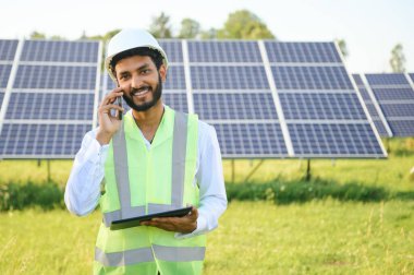 Genç Hintli teknisyen ya da yönetici güneş panelinin yanında duran resmi giysiler giyiyor. Yenilenebilir enerji, çapraz duran adam, boşluğu kopyala.