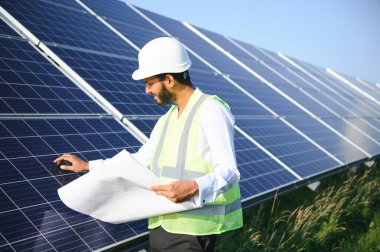 Genç Hintli erkek mühendisin portresi güneş panellerinin yanında duruyor, açık mavi gökyüzü arka planı, yenilenebilir ve temiz enerjisi var. beceri Hindistan, kopyalama alanı
