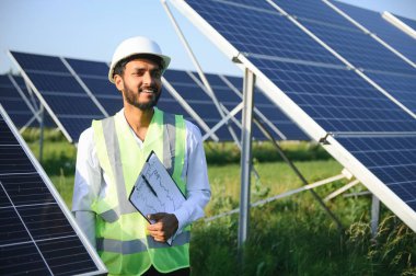 Genç Hintli teknisyen ya da yönetici güneş panelinin yanında duran resmi giysiler giyiyor. Yenilenebilir enerji, çapraz duran adam, boşluğu kopyala.