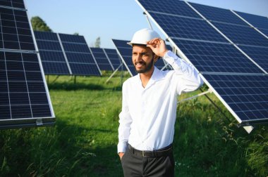 Genç Hintli teknisyen ya da yönetici güneş panelinin yanında duran resmi giysiler giyiyor. Yenilenebilir enerji, çapraz duran adam, boşluğu kopyala.