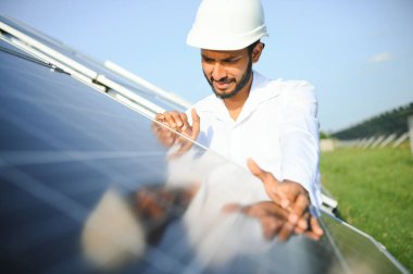 Genç Hintli erkek mühendisin portresi güneş panellerinin yanında duruyor, açık mavi gökyüzü arka planı, yenilenebilir ve temiz enerjisi var. beceri Hindistan, kopyalama alanı