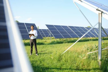 Genç Hintli erkek mühendisin portresi güneş panellerinin yanında duruyor, açık mavi gökyüzü arka planı, yenilenebilir ve temiz enerjisi var. beceri Hindistan, kopyalama alanı