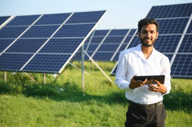 Genç Hintli teknisyen ya da yönetici güneş panelinin yanında duran resmi giysiler giyiyor. Yenilenebilir enerji, çapraz duran adam, boşluğu kopyala.